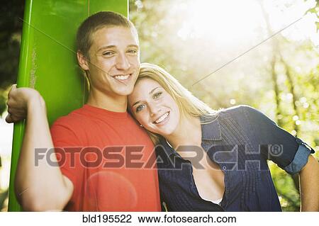 Stock Image - Smiling Caucasian teenage couple with surfboard. Fotosearch