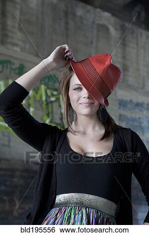Stock Photograph - Smiling Caucasian teenage girl tipping hat on head. Fotosearch