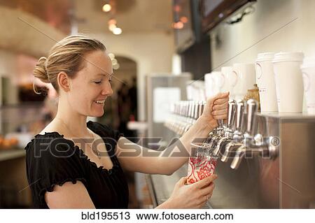 Stock Image - Smiling Caucasian woman filling cup from dispenser. Fotosearch