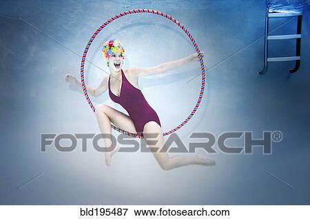 Stock Photo - Smiling Caucasian woman holding plastic hoop and wearing vintage bathing suit and cap underwater. Fotosearch
