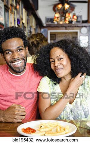 Stock Image - Smiling couple eating french fries in diner. Fotosearch