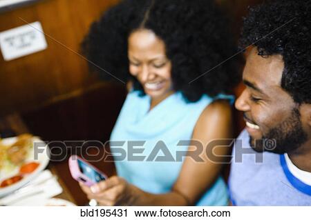 Stock Image - Smiling couple looking at cell phone in diner. Fotosearch