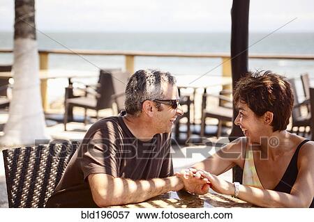 Smiling couple sitting on resort patio holding hands View Large Photo Image Stock Photo - Smiling couple sitting on resort patio holding hands. Fotosearch