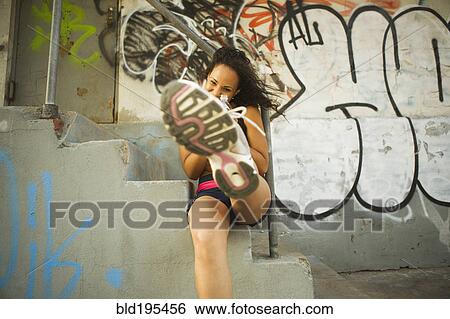 Stock Photograph - Smiling Hispanic woman on urban stairs kicking at camera. Fotosearch