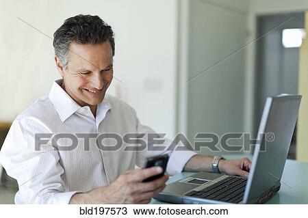 Stock Image - Smiling man text messaging on cell phone. Fotosearch