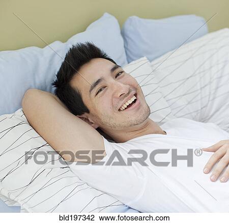 Stock Image - Smiling mixed race man laying in bed. Fotosearch