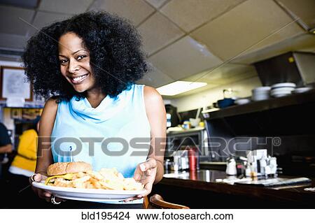 Smiling mixed race waitress holding plate of food in diner View Large Photo Image Picture - Smiling mixed race waitress holding plate of food in diner. Fotosearch