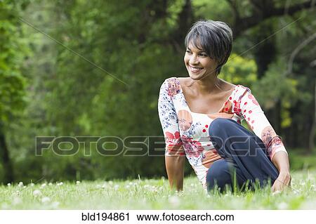 Stock Image - Smiling mixed race woman sitting in field. Fotosearch