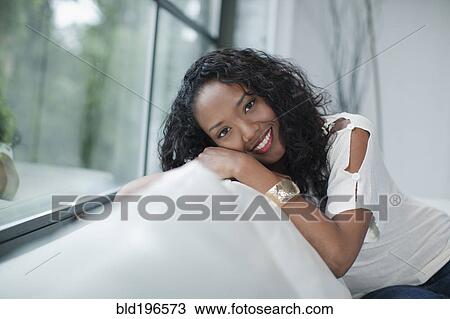 Smiling mixed race woman sitting on sofa View Large Photo Image Stock Image - Smiling mixed race woman sitting on sofa. Fotosearch