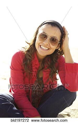 Stock Image - Smiling mixed race woman sitting on beach. Fotosearch