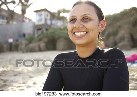 Stock Image - Smiling mixed race woman sitting on beach. Fotosearch
