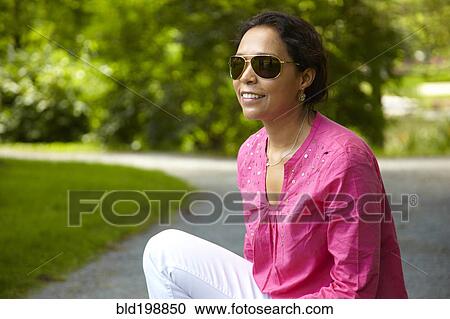 Stock Image - Smiling mixed race woman sitting outdoors. Fotosearch