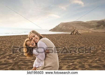 Stock Image - Smiling mother and daughter hugging on beach. Fotosearch