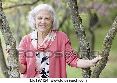 Picture - Smiling senior Caucasian woman standing near tree. Fotosearch