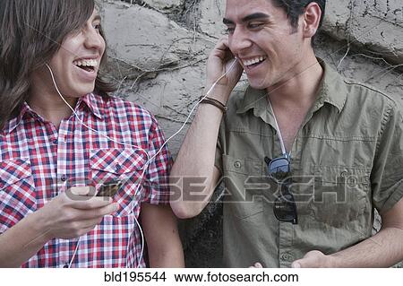Picture - Smiling teenage boys sharing headphones and holding mp3 player. Fotosearch
