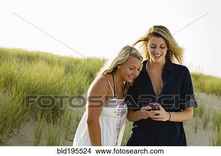 Smiling teenage girls text messaging with cell phone on beach View Large Photo Image Picture - Smiling teenage girls text messaging with cell phone on beach. Fotosearch
