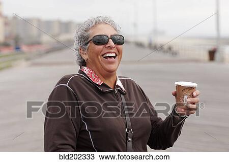 Stock Image - Smiling woman drinking coffee on boardwalk. Fotosearch