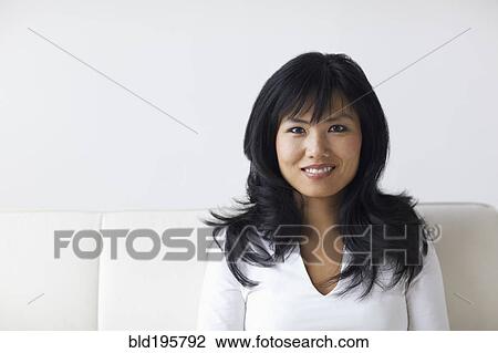Stock Image - Smiling woman sitting on sofa. Fotosearch