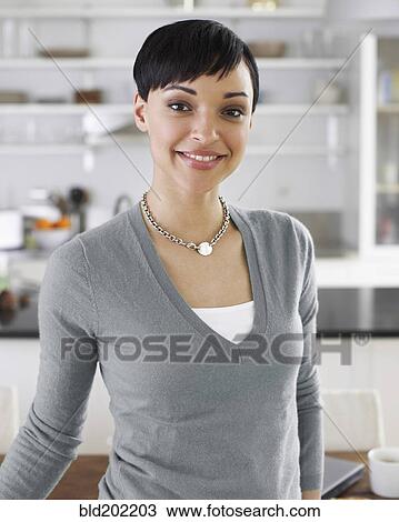 Stock Image - Smiling woman standing in kitchen. Fotosearch