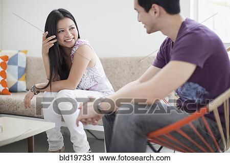 Stock Image - Smiling woman talking to husband in living room. Fotosearch