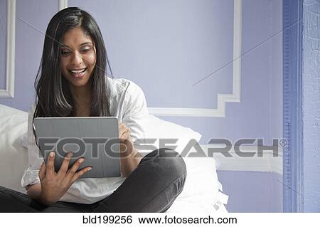 Stock Photograph - Sri Lankan woman on bed using digital tablet. Fotosearch