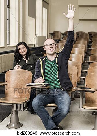 Stock Image - Student raising his hand in classroom. Fotosearch