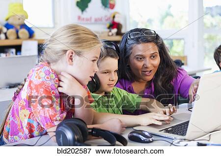 Stock Photo - Teacher helping students using laptop. Fotosearch