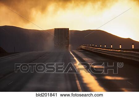 Stock Image - Truck driving down road on wet highway. Fotosearch