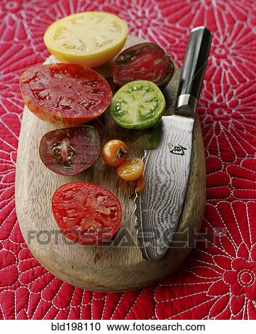 Stock Image - Various juicy sliced tomatoes on cutting board with knife. Fotosearch
