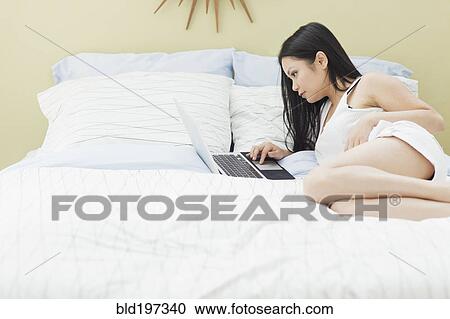 Stock Image - Vietnamese woman using laptop in bed. Fotosearch