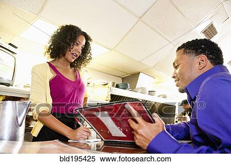 Stock Photography - Waitress taking order from man with menu at diner counter. Fotosearch