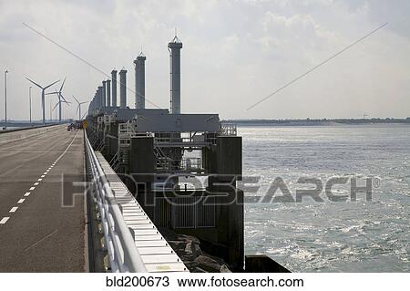 Stock Image - Wind turbines and dam across ocean. Fotosearch