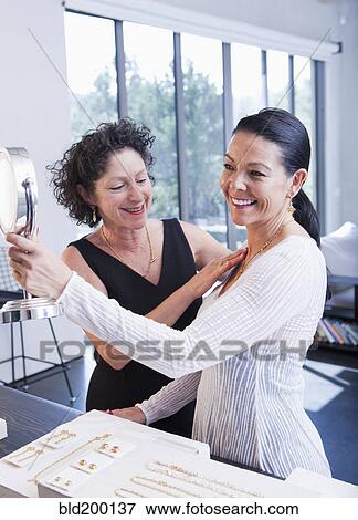 Stock Photo - Woman helping customer try in jewelry in store. Fotosearch
