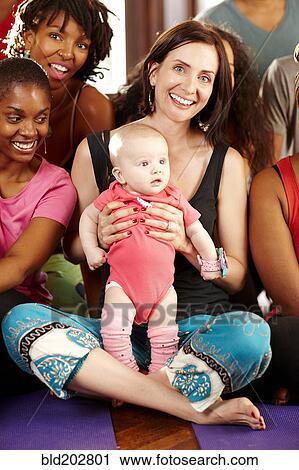 Stock Image - Woman holding baby in yoga class. Fotosearch