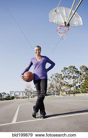 Stock Photo - Woman holding basketball on basketball court. Fotosearch