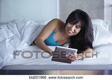 Woman laying in bed using digital tablet View Large Photo Image Stock Photograph - Woman laying in bed using digital tablet. Fotosearch