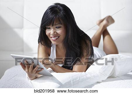 Stock Photo - Woman laying on bed using digital tablet. Fotosearch