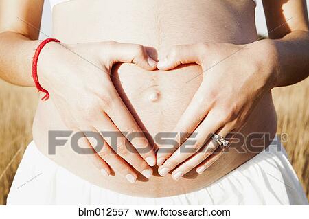 Stock Photo - Woman making heart-shape with hands on pregnant stomach. Fotosearch