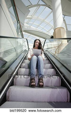 Stock Image - Woman on escalator using digital tablet. Fotosearch