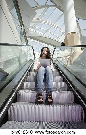 Stock Image - Woman on escalator using digital tablet. Fotosearch