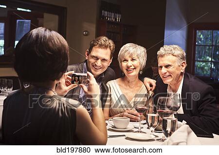 Stock Image - Woman photographing friends in restaurant. Fotosearch
