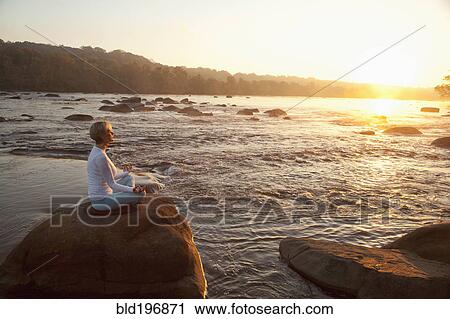 Stock Image - Woman practicing yoga on rock near ocean. Fotosearch