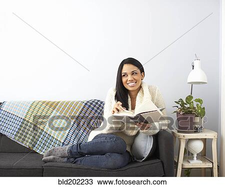 Stock Image - Woman reading book on sofa. Fotosearch
