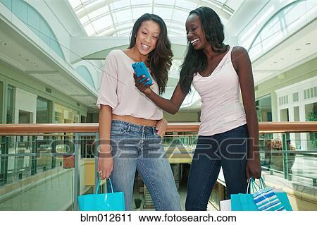 Stock Image - Woman showing cell to friend in shopping mall. Fotosearch