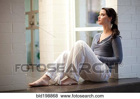 Stock Photo - Woman sitting on floor leaning on wall. Fotosearch