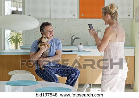 Woman taking picture of husband holding dog in kitchen View Large Photo Image Stock Photo - Woman taking picture of husband holding dog in kitchen. Fotosearch