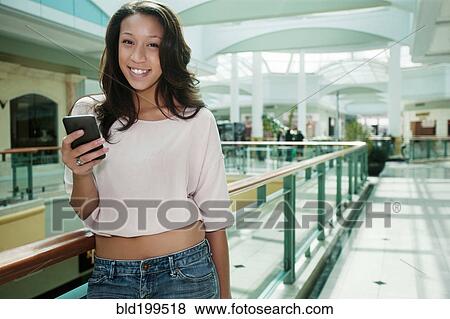 Stock Photo - Woman text messaging on cell phone in shopping mall. Fotosearch