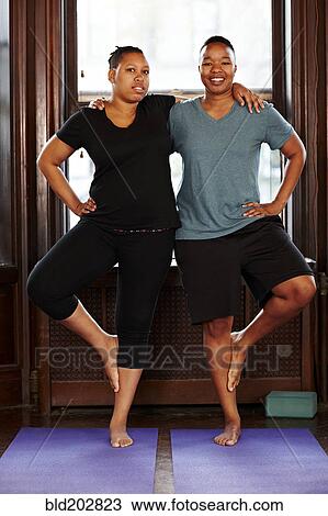 Stock Image - Women balancing together in yoga class. Fotosearch