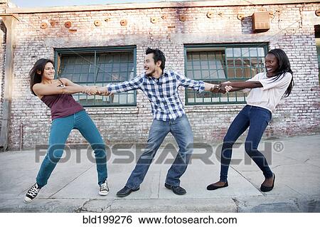 Stock Photograph - Women pulling on male friend's arms. Fotosearch