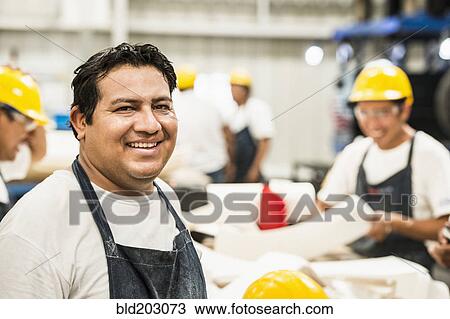 Stock Image - Worker smiling in manufacturing plant. Fotosearch